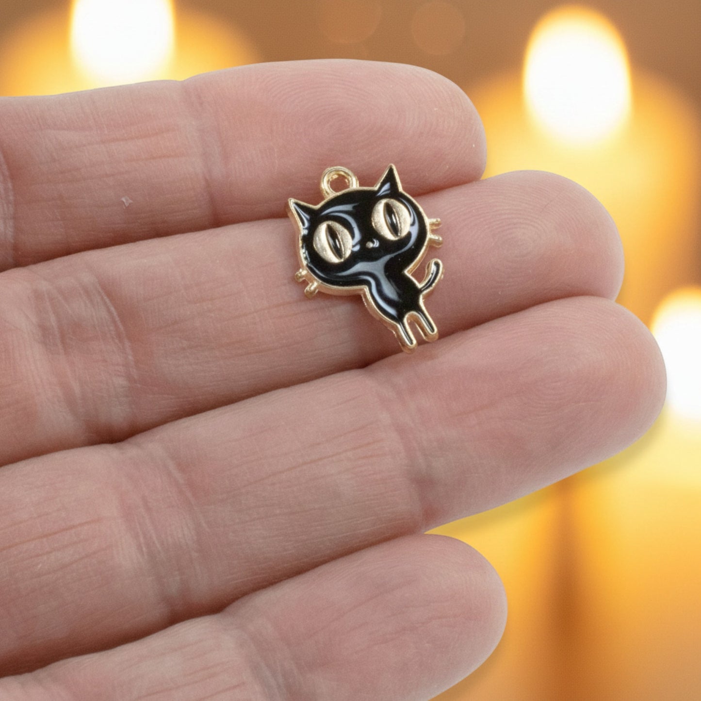 Hackberry Creek black enamel cat charm with gold-plated metal alloy held between fingers for jewelry making