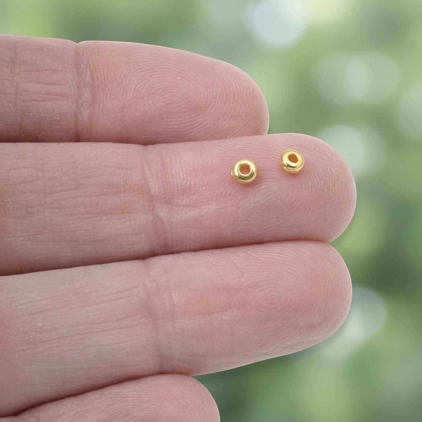 Hackberry Creek 3mm gold heishi disc spacer beads made of 24K-plated pewter, shown on fingers.