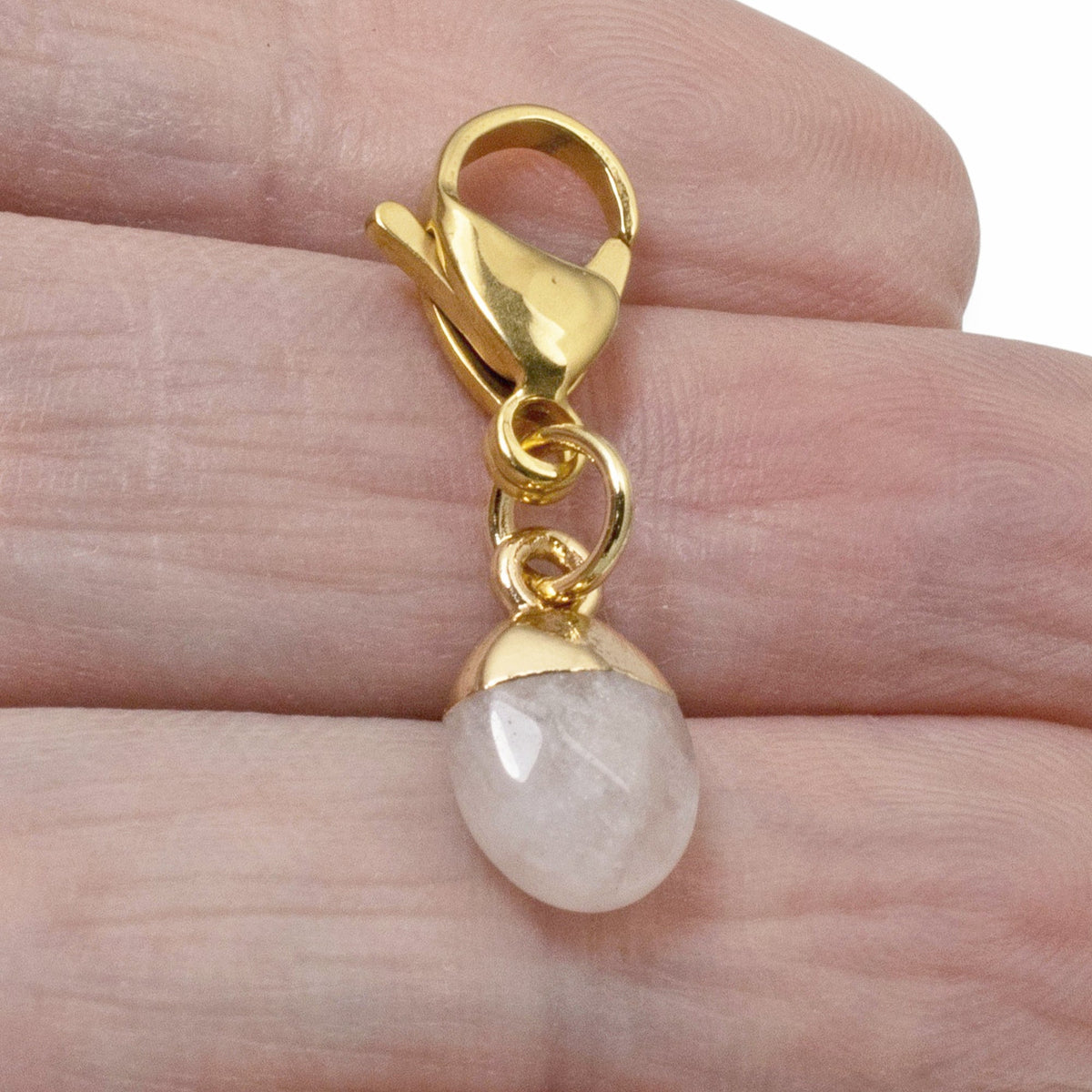 Hackberry Creek dainty oval rose quartz charm with a gold-plated stainless steel clasp held in a hand.