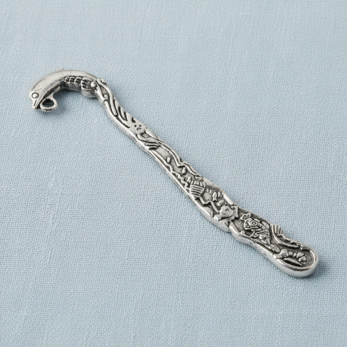 Hackberry Creek antique silver dolphin bookmark with beach-themed engraving and charm loop on a light blue background.