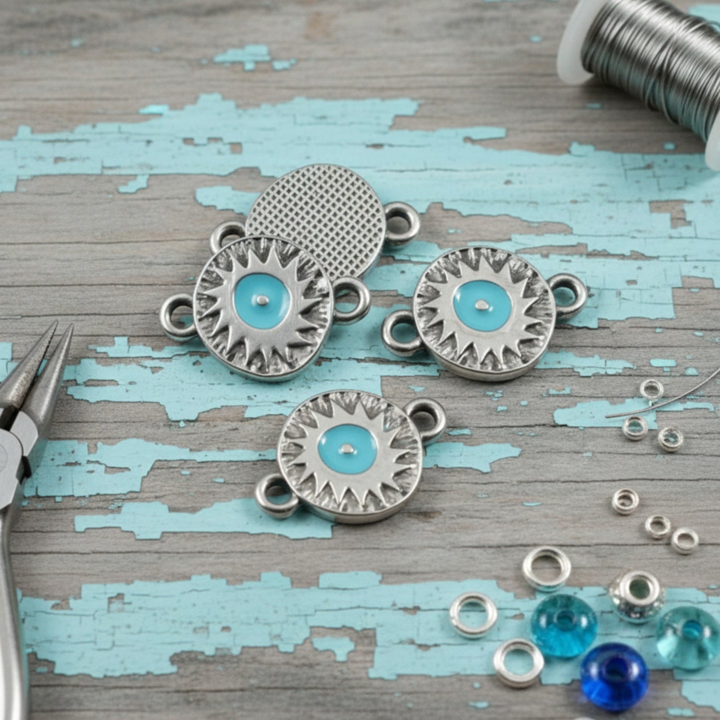 Hackberry Creek antique silver evil eye connector charms with aqua enamel centers on a rustic blue wooden background.