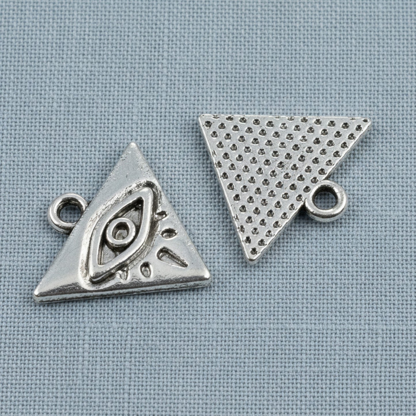 Hackberry Creek antique silver triangle evil eye charms for mystical jewelry making on a blue fabric background