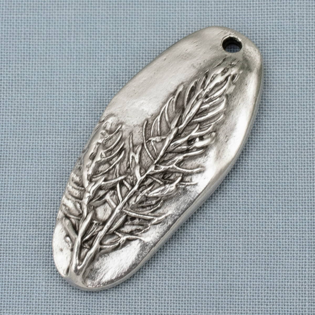 Hackberry Creek antique silver Denali pine tree pendant with detailed embossed forest design on a grey fabric background
