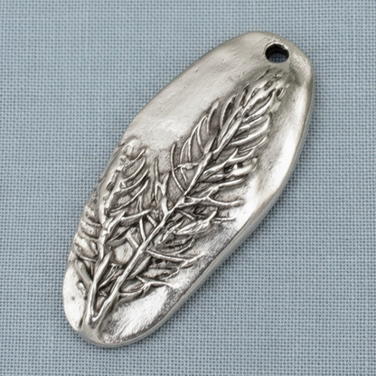 Hackberry Creek antique silver Denali pine tree pendant with detailed embossed forest design on a grey fabric background