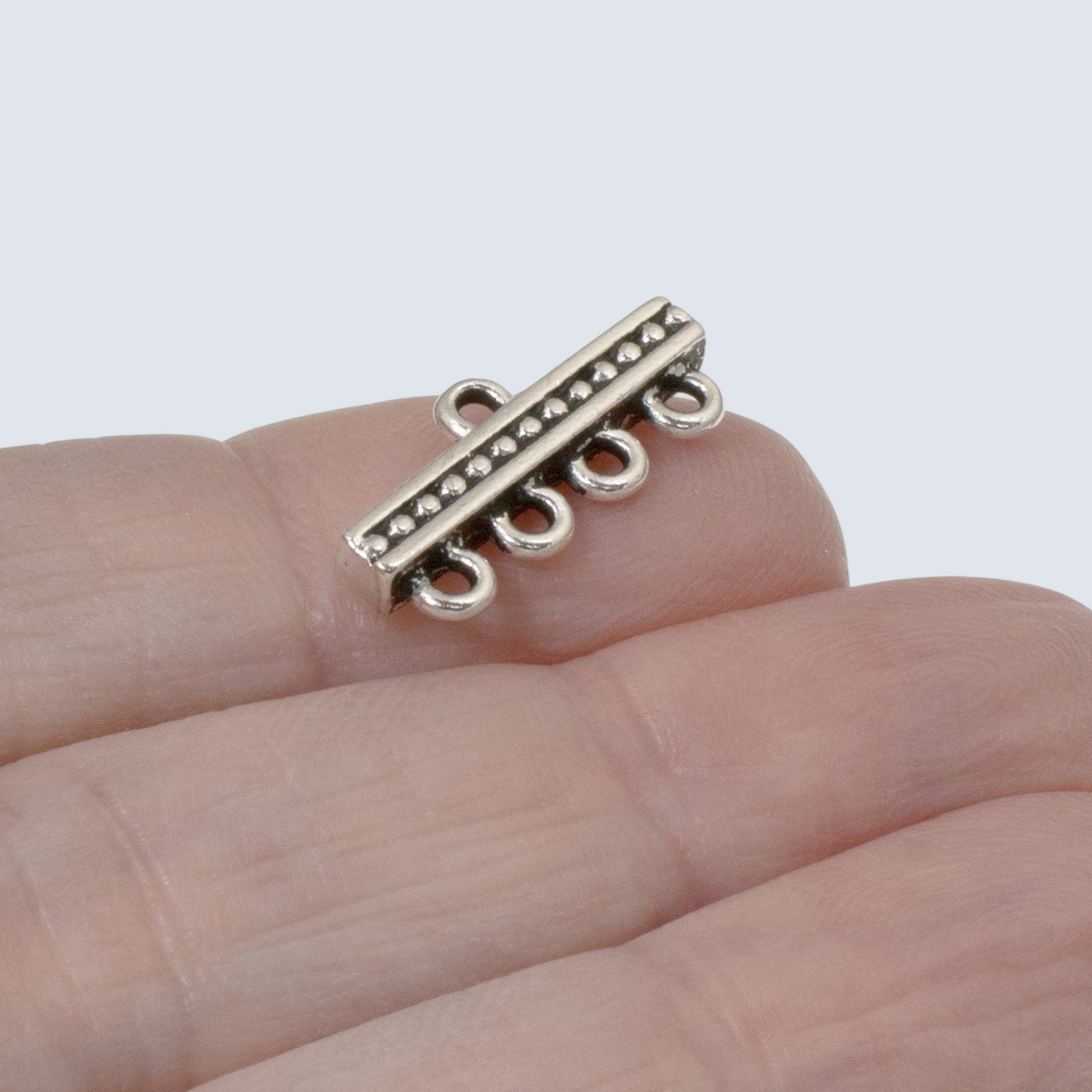 Hackberry Creek silver-plated 4-to-1 beaded connector link held on a finger for jewelry making