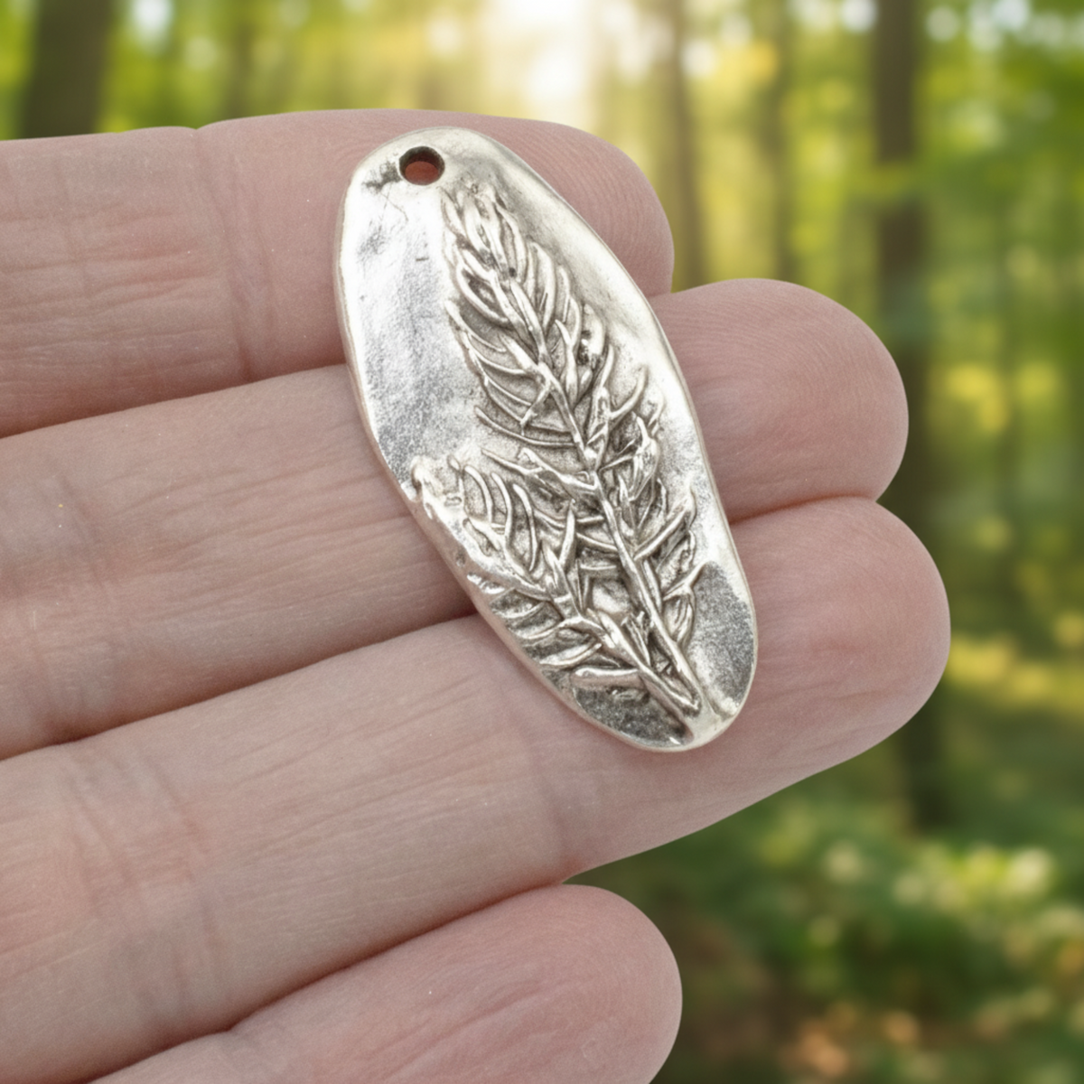Hackberry Creek antique silver Denali pine tree pendant held in hand against a blurred forest background.