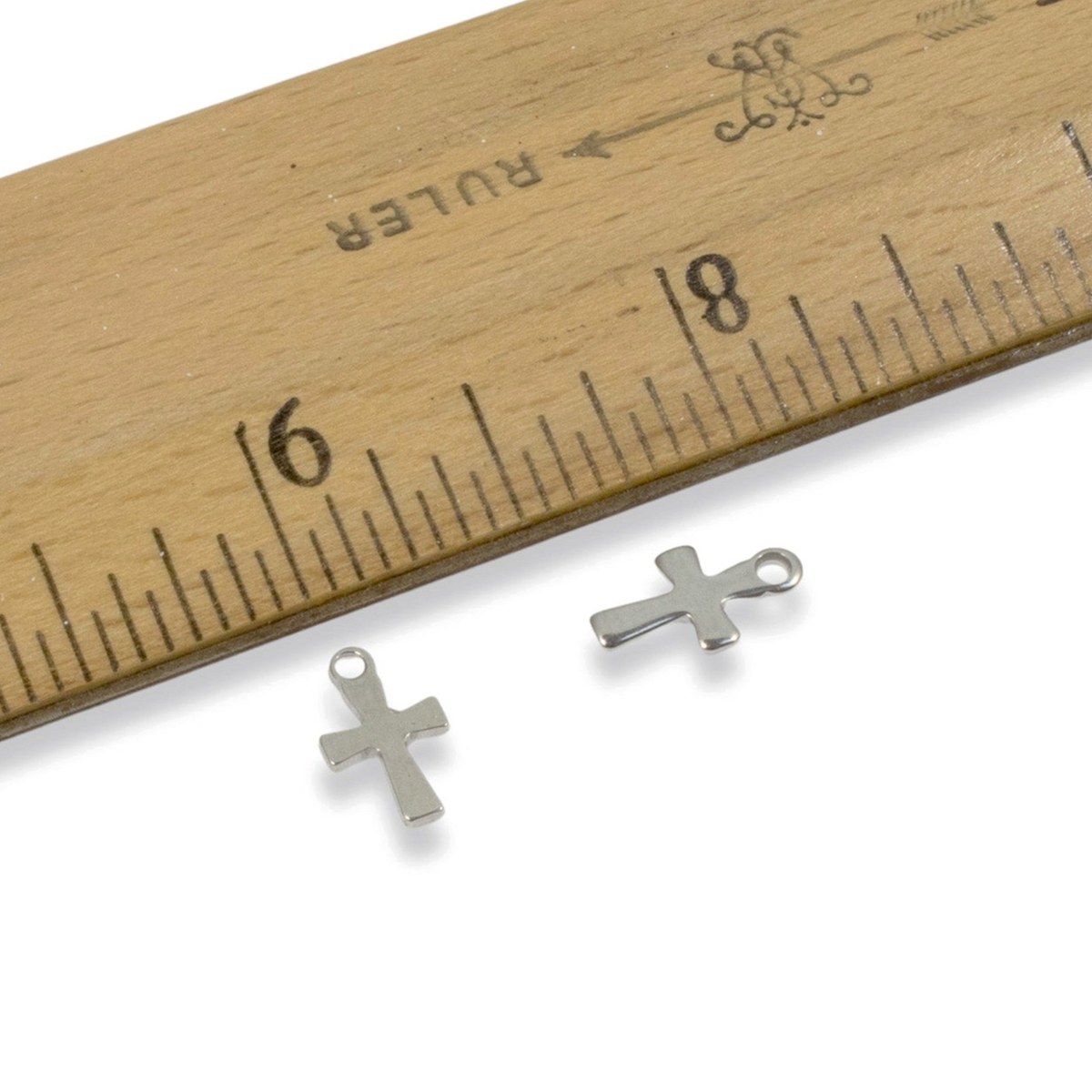Hackberry Creek stainless steel mini cross charms for jewelry making, shown next to a wooden ruler for scale.