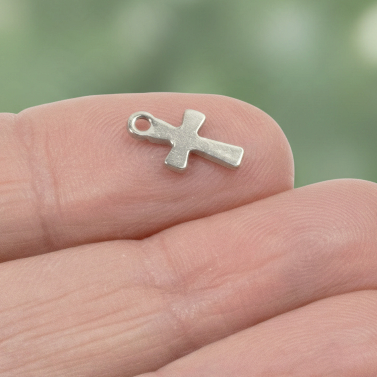 Hackberry Creek mini silver stainless steel cross charm held on a fingertip for scale