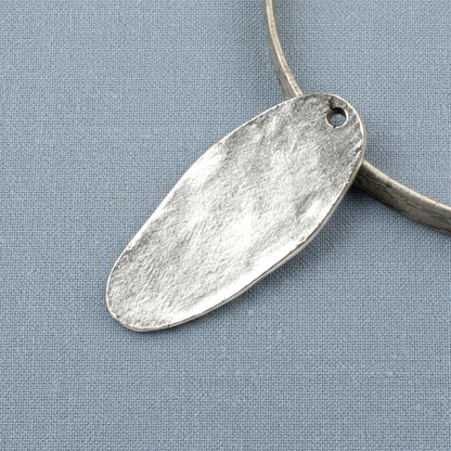 Hackberry Creek antique silver tree pendant showing the smooth, plain back side on a textured blue fabric background.