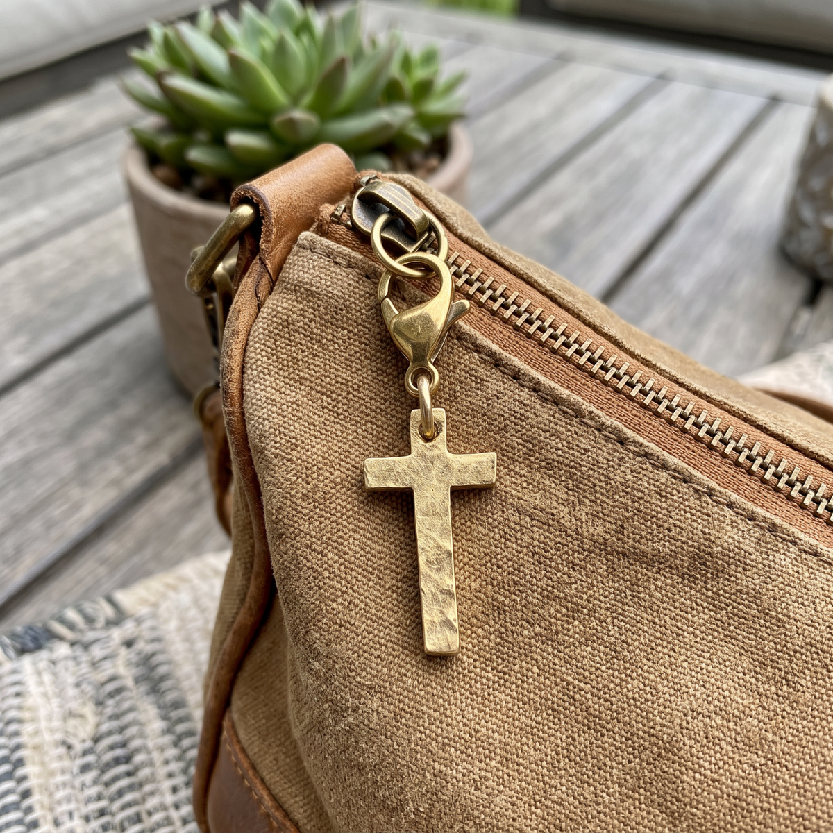 Hackberry Creek gold-plated hammered cross charm clipped onto a brown canvas purse zipper pull.