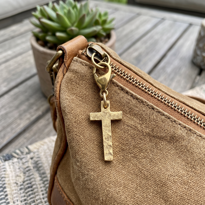 Hackberry Creek gold-plated hammered cross charm clipped onto a brown canvas purse zipper pull.