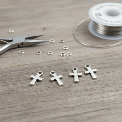 Hackberry Creek stainless steel mini cross charms for jewelry making on a wooden surface with pliers and wire