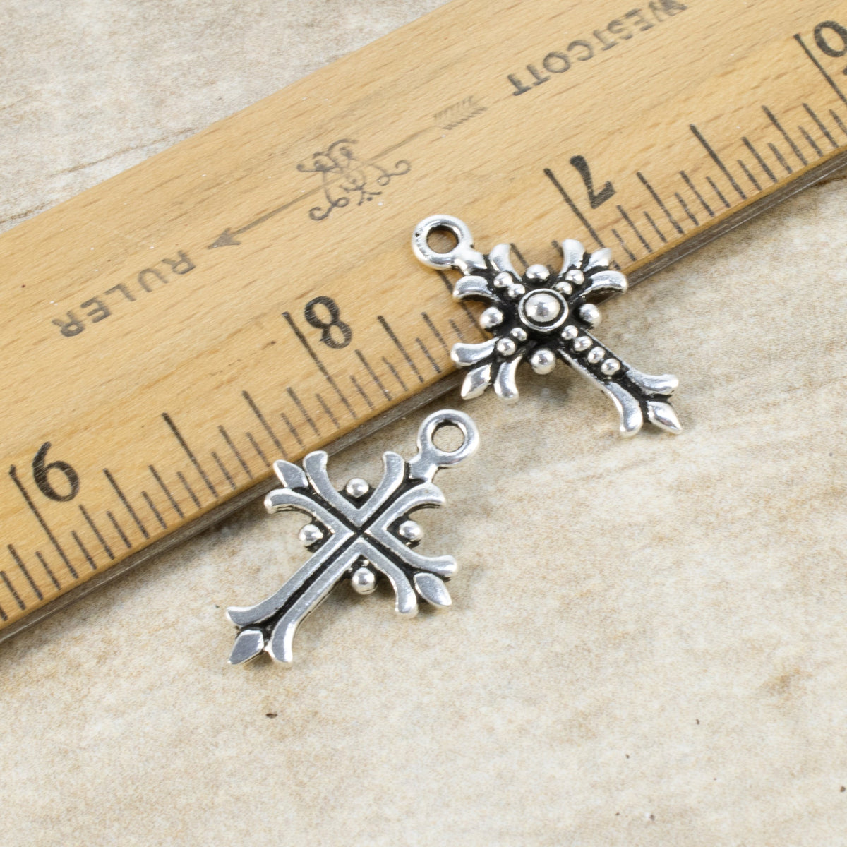 Hackberry Creek antique silver fleur cross charms with raised relief detail, shown next to a ruler for scale.