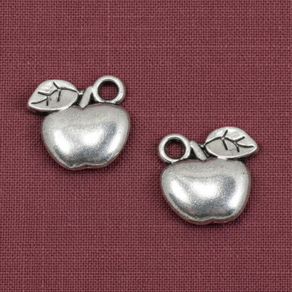 Hackberry Creek silver apple charms for jewelry making, featuring a durable zinc alloy design on a maroon background.