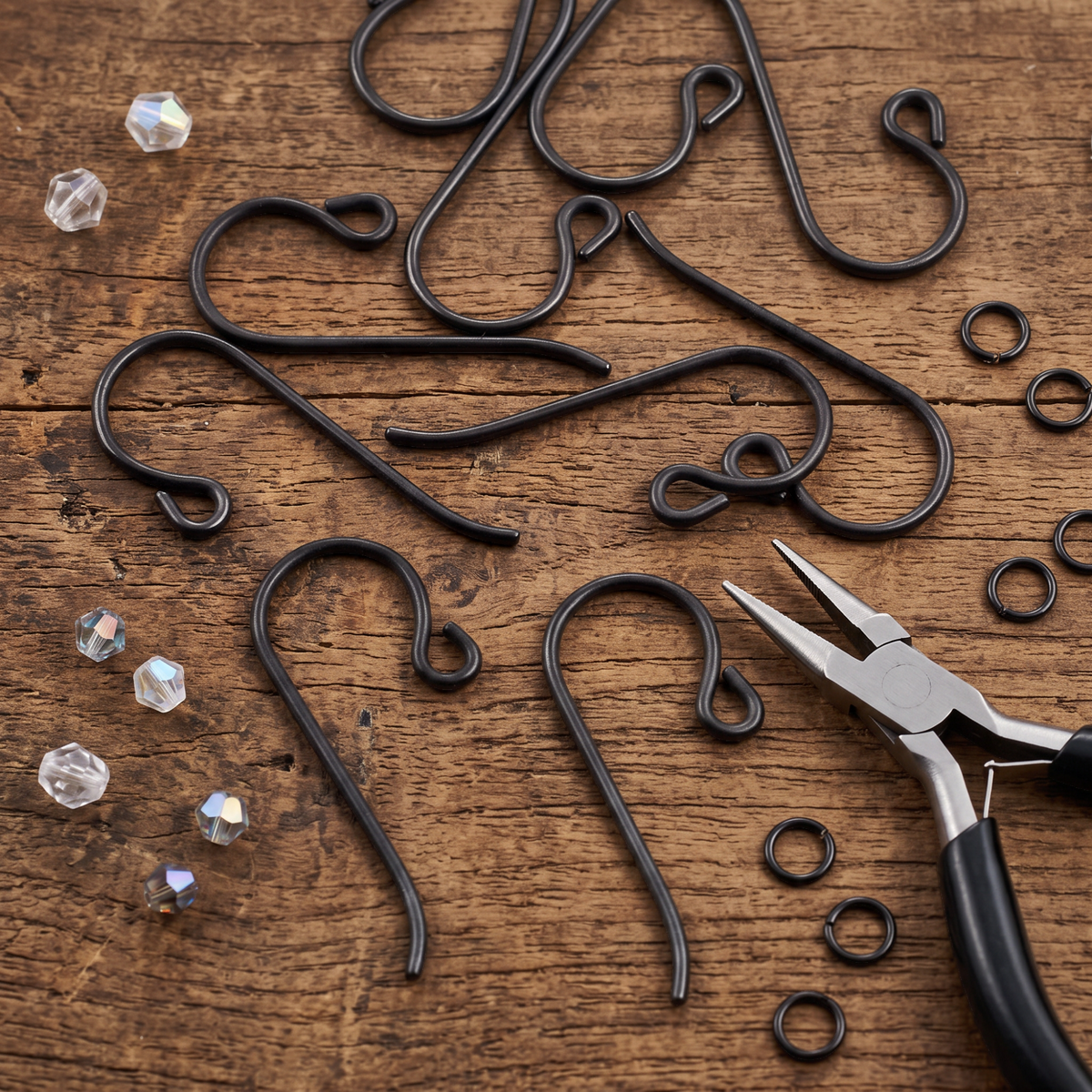 Hackberry Creek black niobium French hook ear wires with small loops and jewelry pliers on a rustic wooden surface.