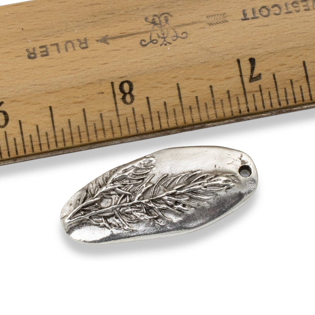 Hackberry Creek antique silver Denali pine tree pendant with detailed forest design next to a wooden ruler