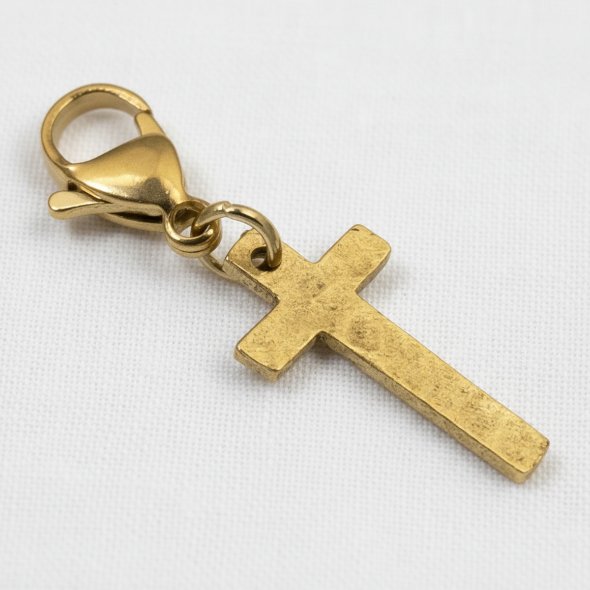 Hackberry Creek gold cross charm with a hammered finish and stainless steel lobster clasp on a white background.