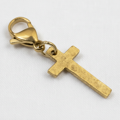Hackberry Creek gold cross charm with a hammered finish and stainless steel lobster clasp on a white background.
