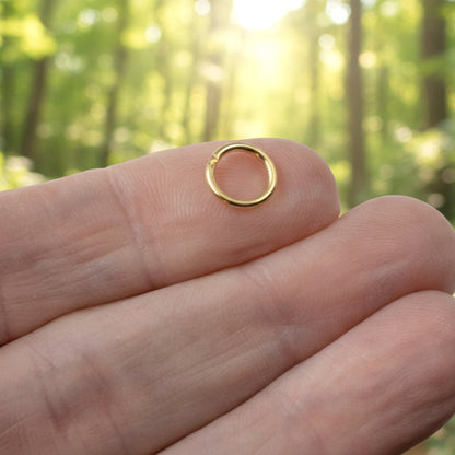 Hackberry Creek 9mm bright gold jump ring made of 304 stainless steel held on a fingertip in a forest setting.