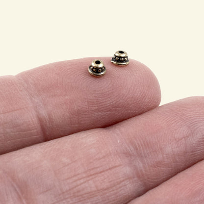 Hackberry Creek antique brass beaded bead caps resting on a fingertip showing tiny rustic vintage-style jewelry parts