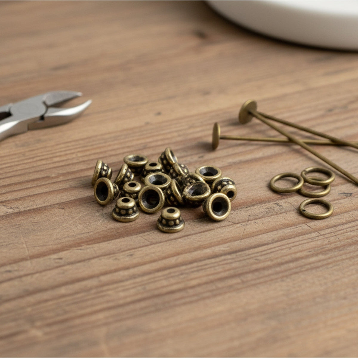 Hackberry Creek antique brass beaded bead caps for jewelry making on a wooden table with tools.