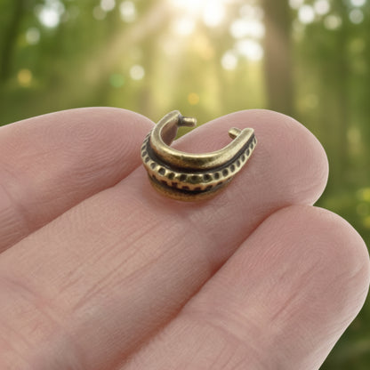 Hackberry Creek antique brass hammered pinch bail held on a finger with a blurred forest background