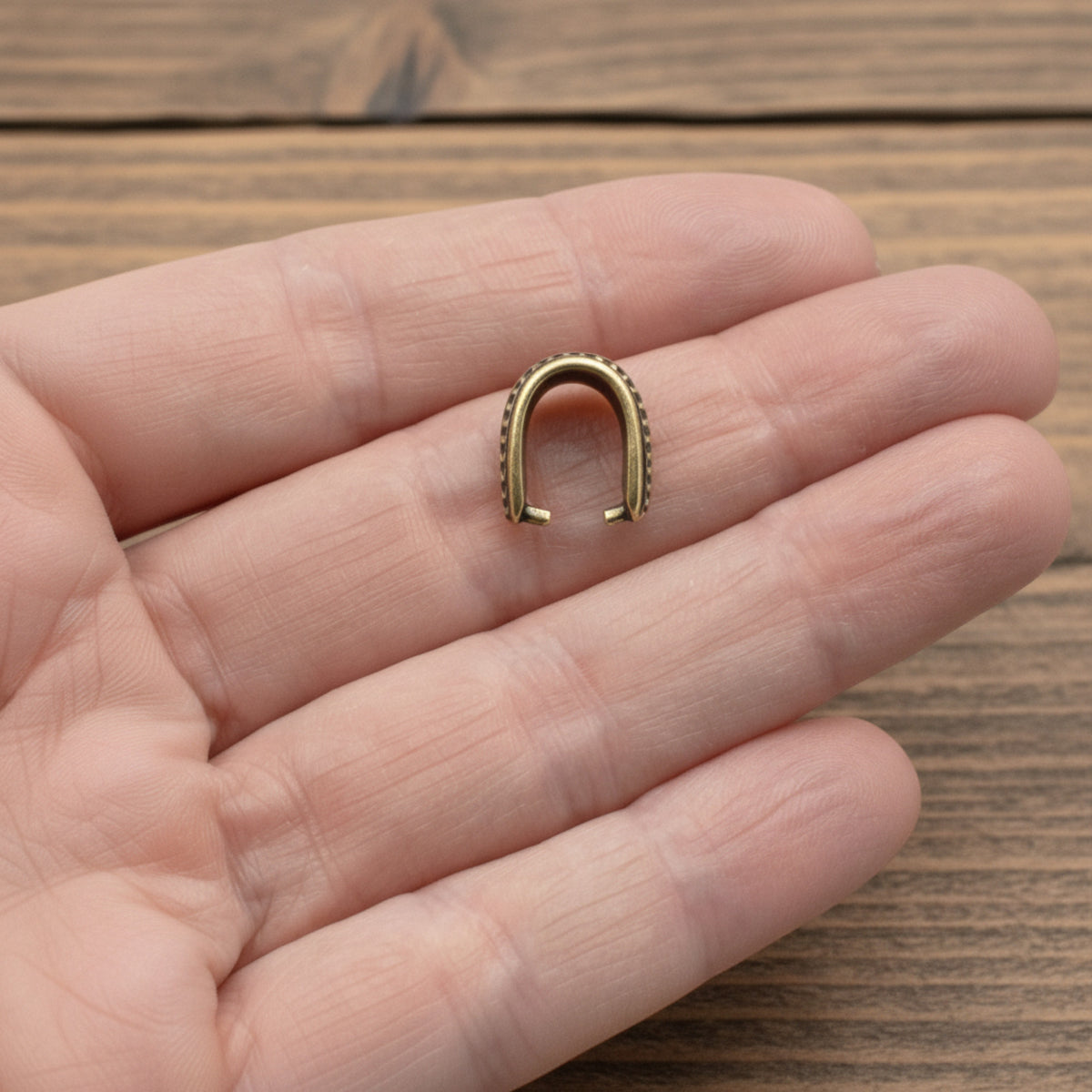 Hackberry Creek antique brass hammered pinch bail held in a palm for scale, showing vintage patina and texture.