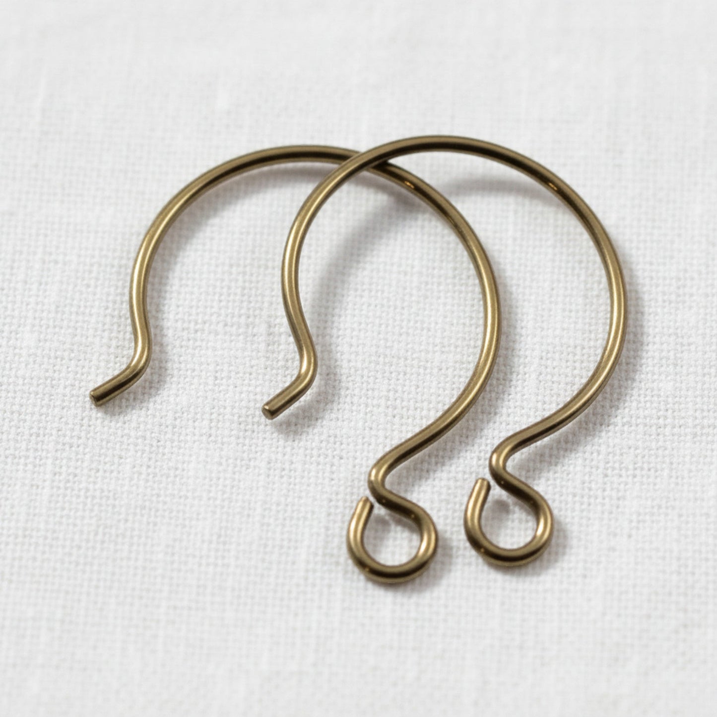 Hackberry Creek antique brass niobium circle hoop ear wires for hypoallergenic jewelry making on white fabric.