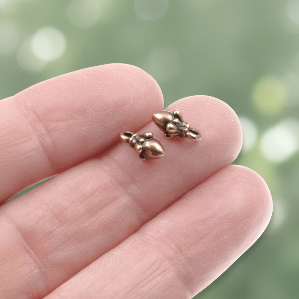Hackberry Creek tiny antique copper acorn charms with 3D sculpted detail held on a fingertip