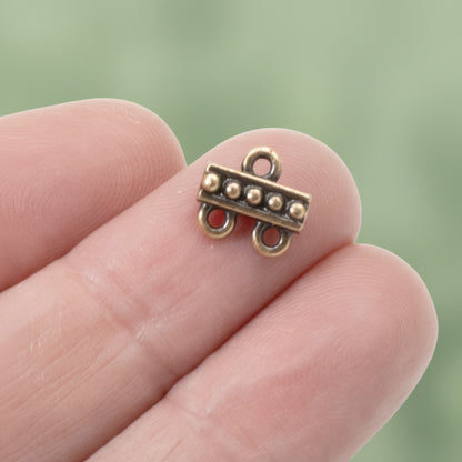 Hackberry Creek antique copper 2:1 beaded jewelry connector held on a finger for scale