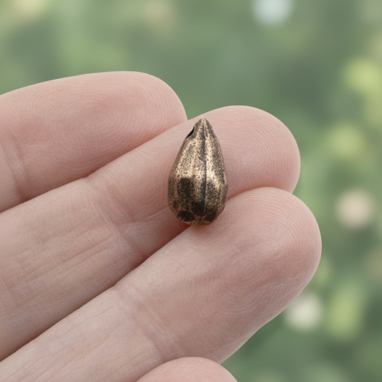 Hackberry Creek faceted drop bead in antique copper-plated pewter held between fingers for scale