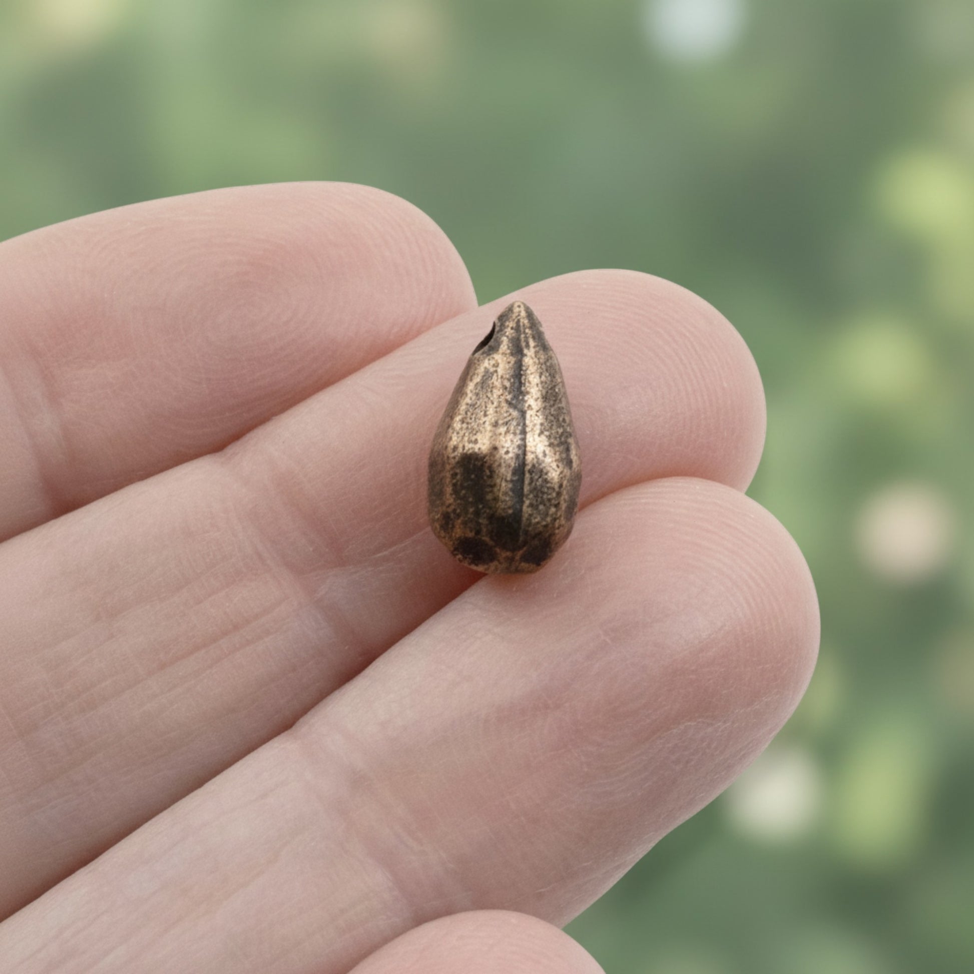 Hackberry Creek faceted drop bead in antique copper-plated pewter held between fingers for scale
