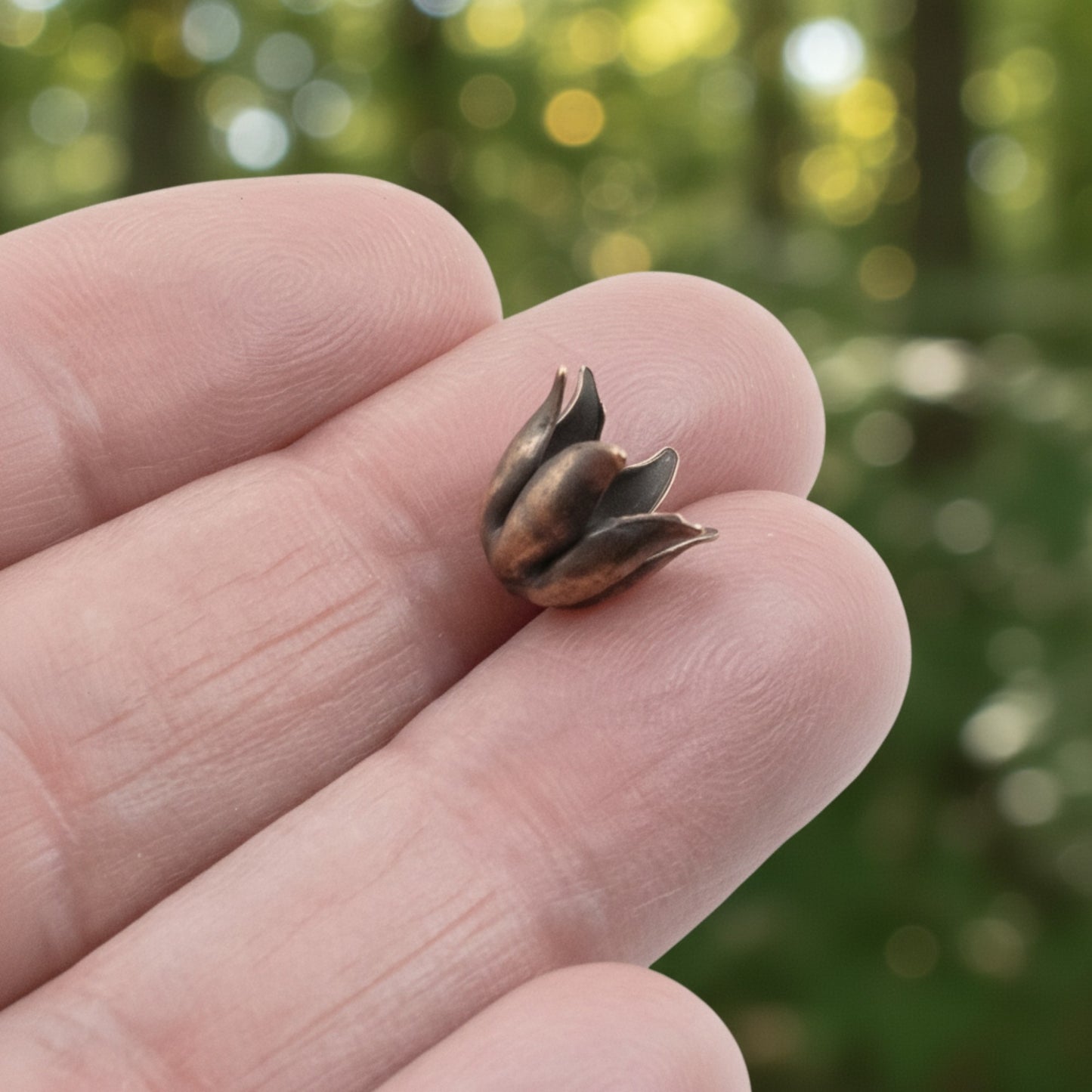 Hackberry Creek antique copper-plated pewter bead cap with a sculptural curled petal design held between fingers.