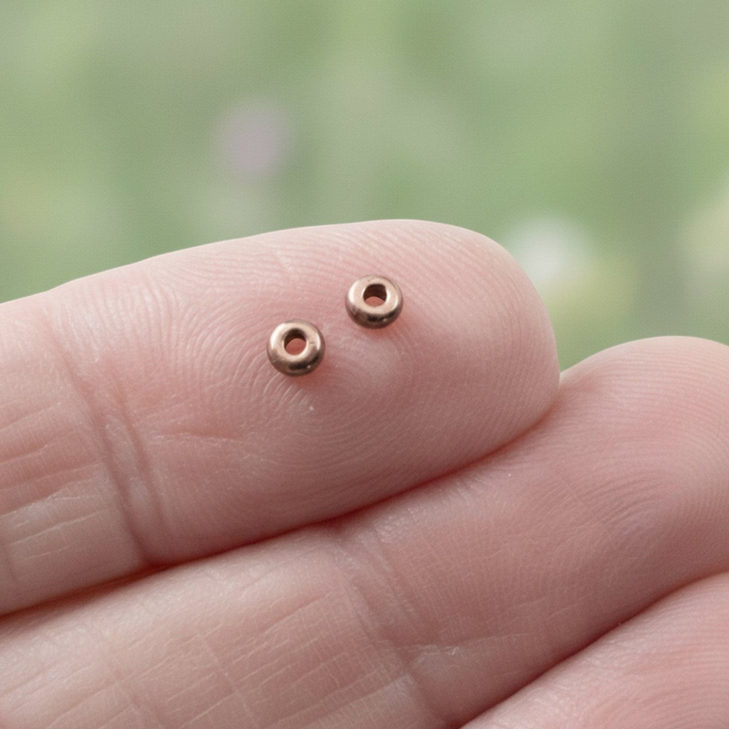Hackberry Creek antique copper 3mm smooth heishi spacer beads on a fingertip.
