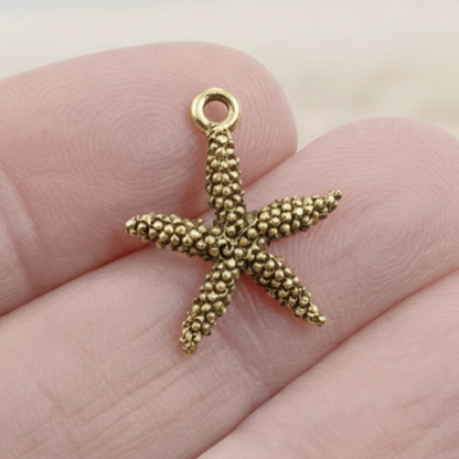 Hackberry Creek antique gold pewter starfish charm with textured surface held between fingers for scale