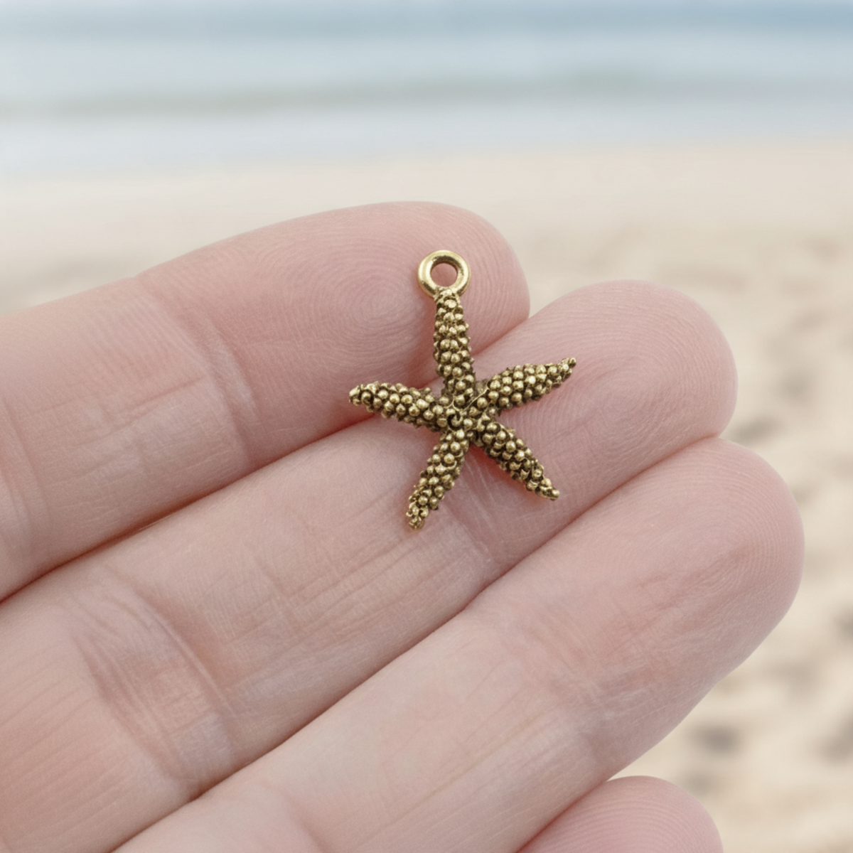 Hackberry Creek antique gold pewter starfish charm held in hand against a blurred beach background