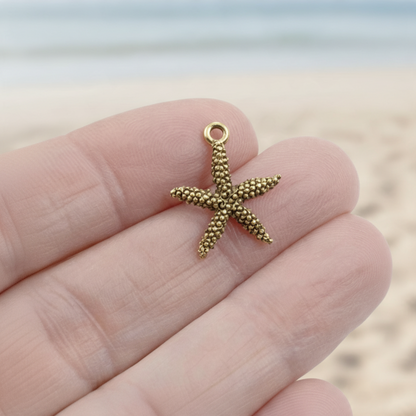 Hackberry Creek antique gold pewter starfish charm held in hand against a blurred beach background
