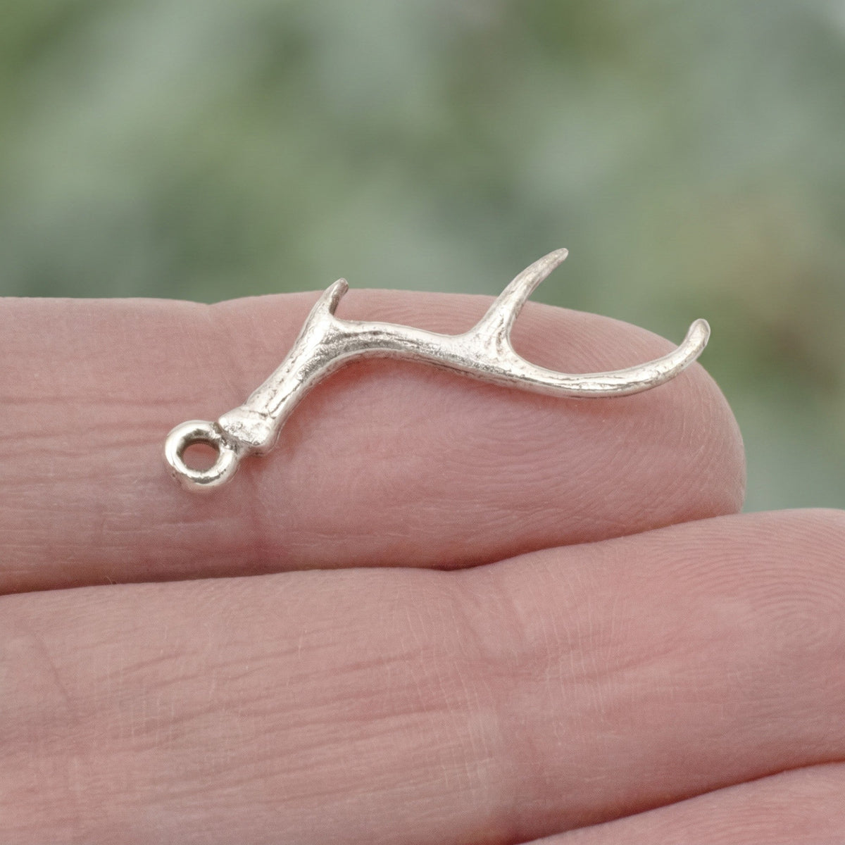 Hackberry Creek antique silver antler charm for jewelry making held on a fingertip