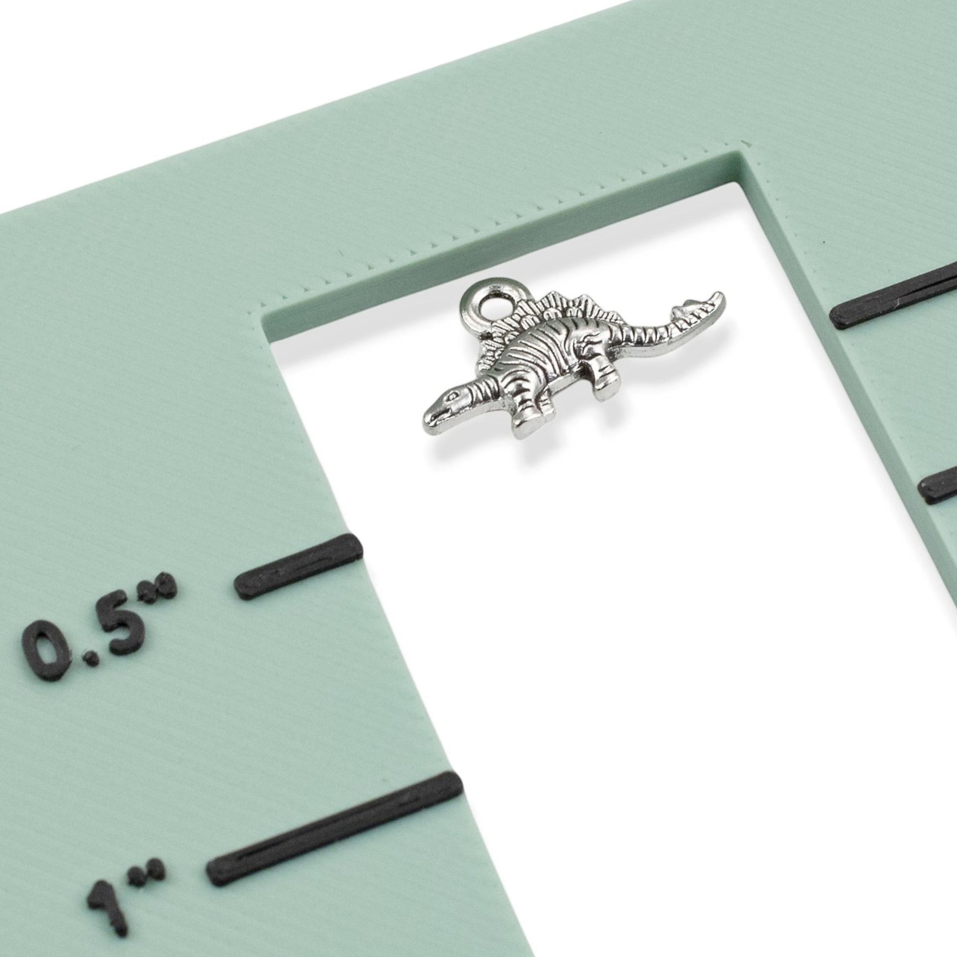 Hackberry Creek antique silver dinosaur charm on a green measuring tool showing scale for jewelry making