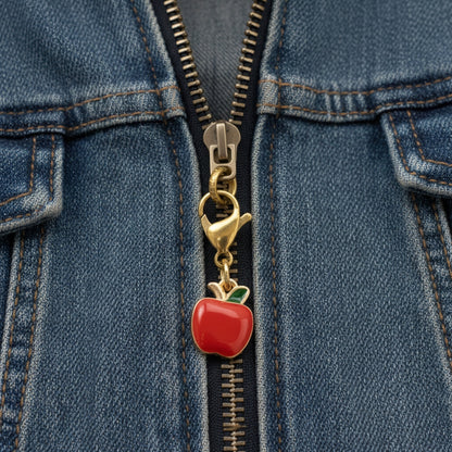 Hackberry Creek gold-plated apple charm with red and green enamel attached to a blue denim jacket zipper.
