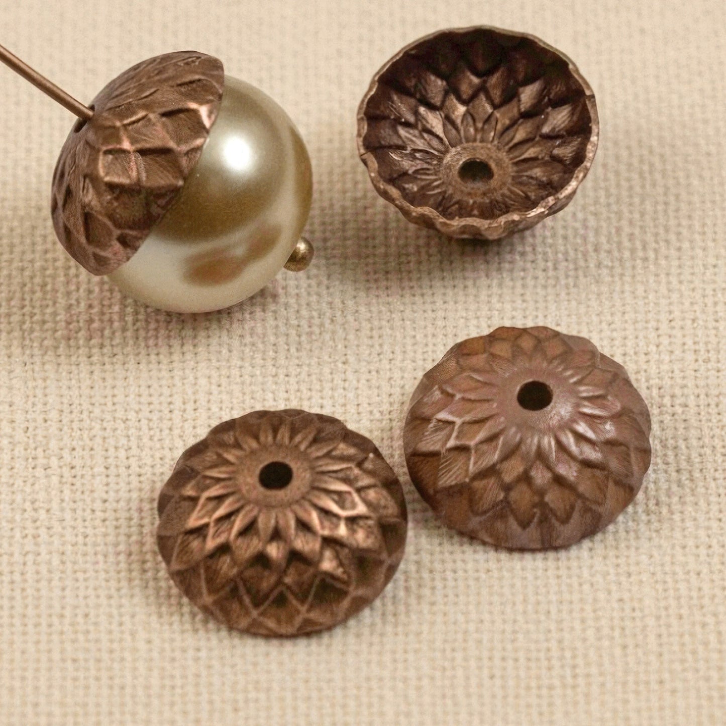 Hackberry Creek 12.5mm artisan copper acorn bead caps with detailed sunflower relief pattern on a textured fabric