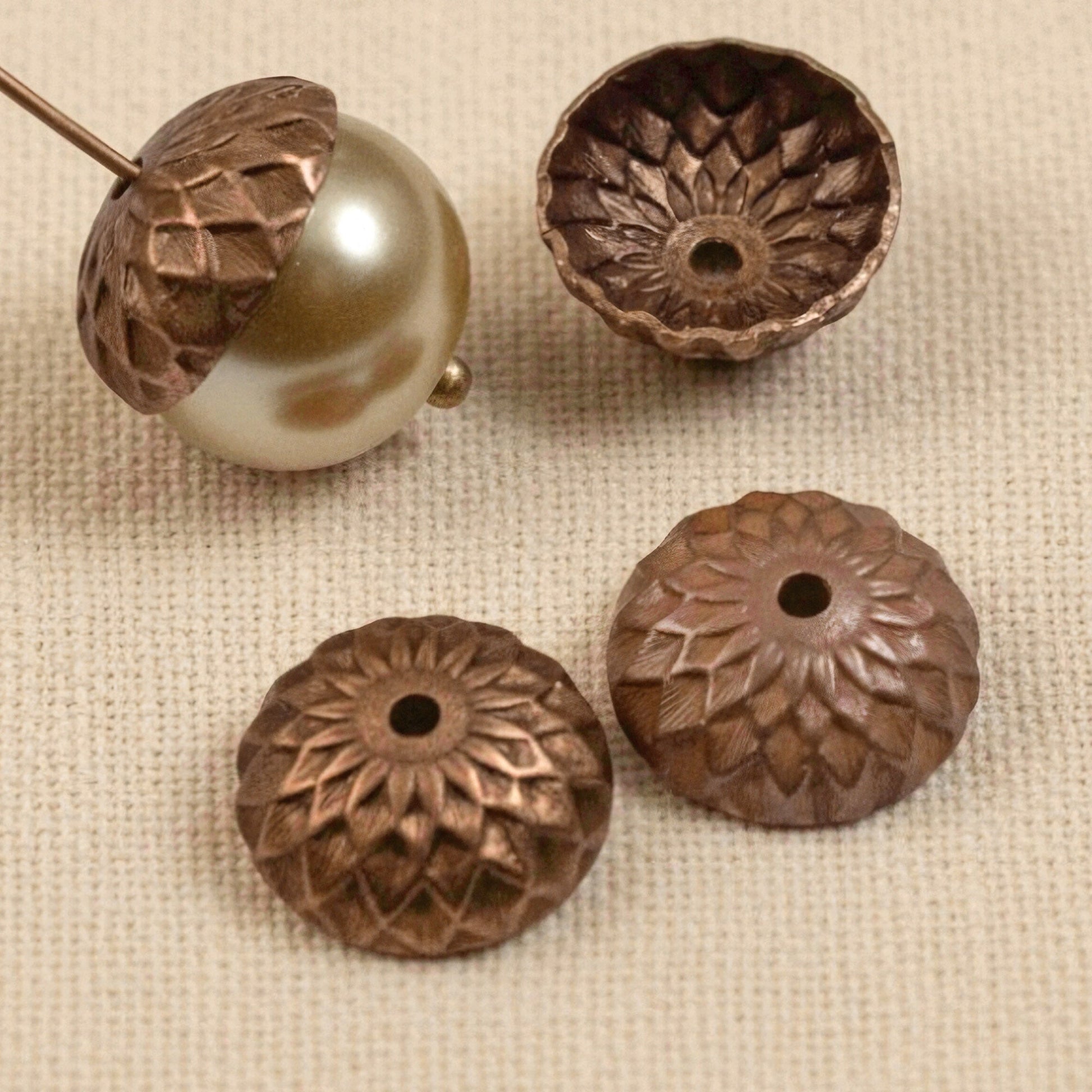 Hackberry Creek 12.5mm artisan copper acorn bead caps with detailed sunflower relief pattern on a textured fabric