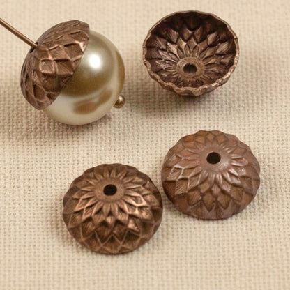 Hackberry Creek 12.5mm artisan copper acorn bead caps with detailed sunflower relief pattern on a textured fabric