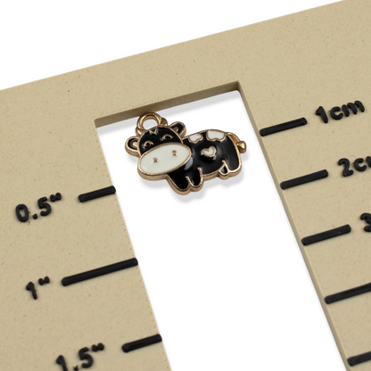 Hackberry Creek black and ivory enamel cow charm with copper outline on a measurement scale for size reference.