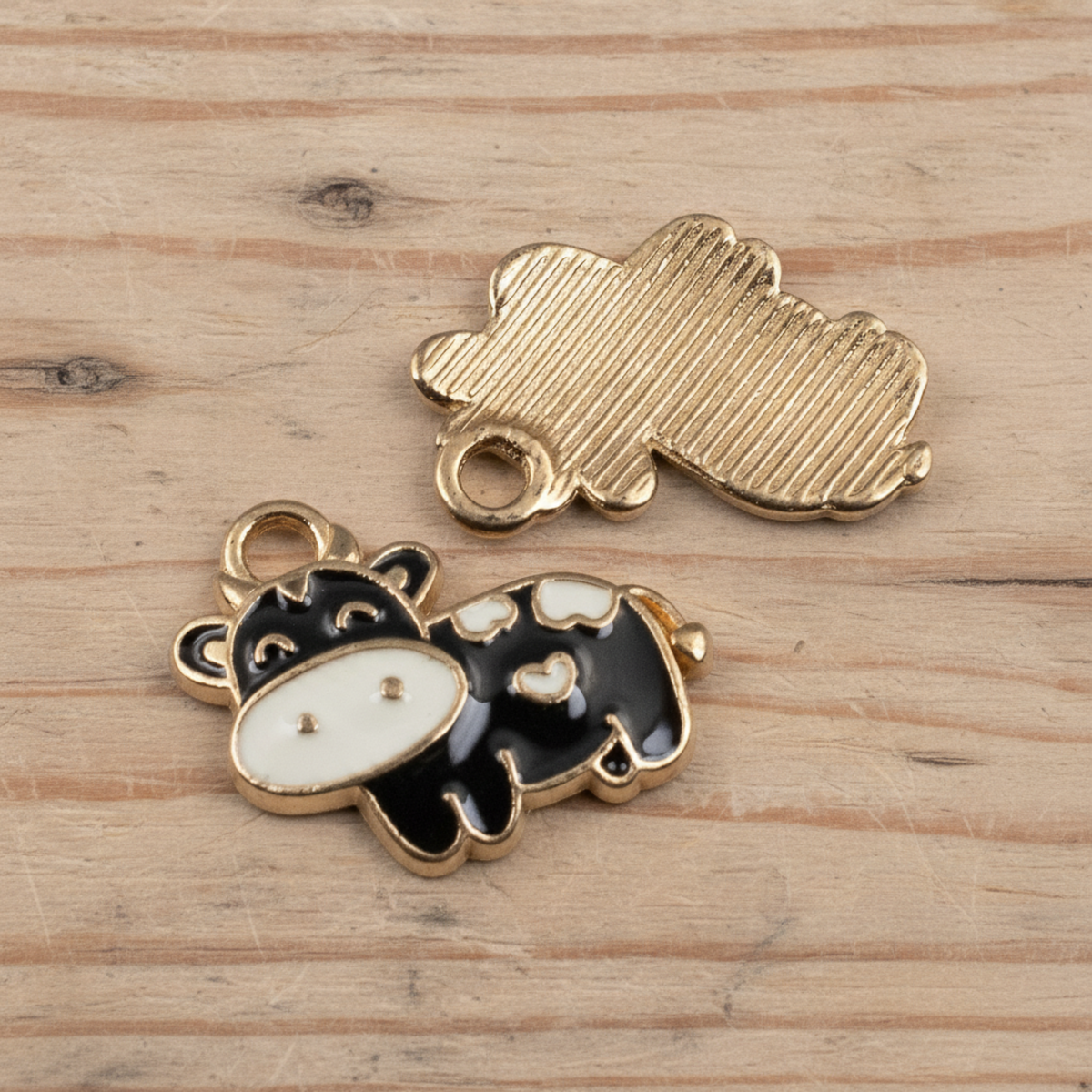 Hackberry Creek black and ivory enamel cow charms with copper outline and textured copper back on a wooden surface.