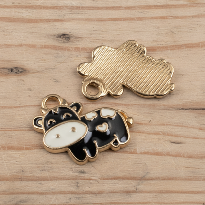 Hackberry Creek black and ivory enamel cow charms with copper outline and textured copper back on a wooden surface.