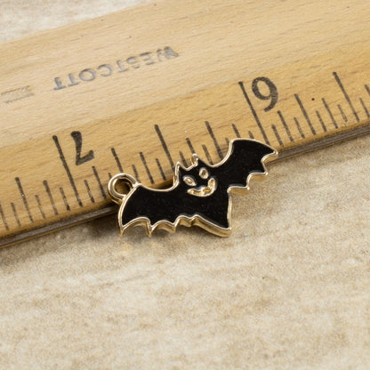 Hackberry Creek black enamel flying bat charm with gold trim next to a ruler for scale, ideal for gothic jewelry.