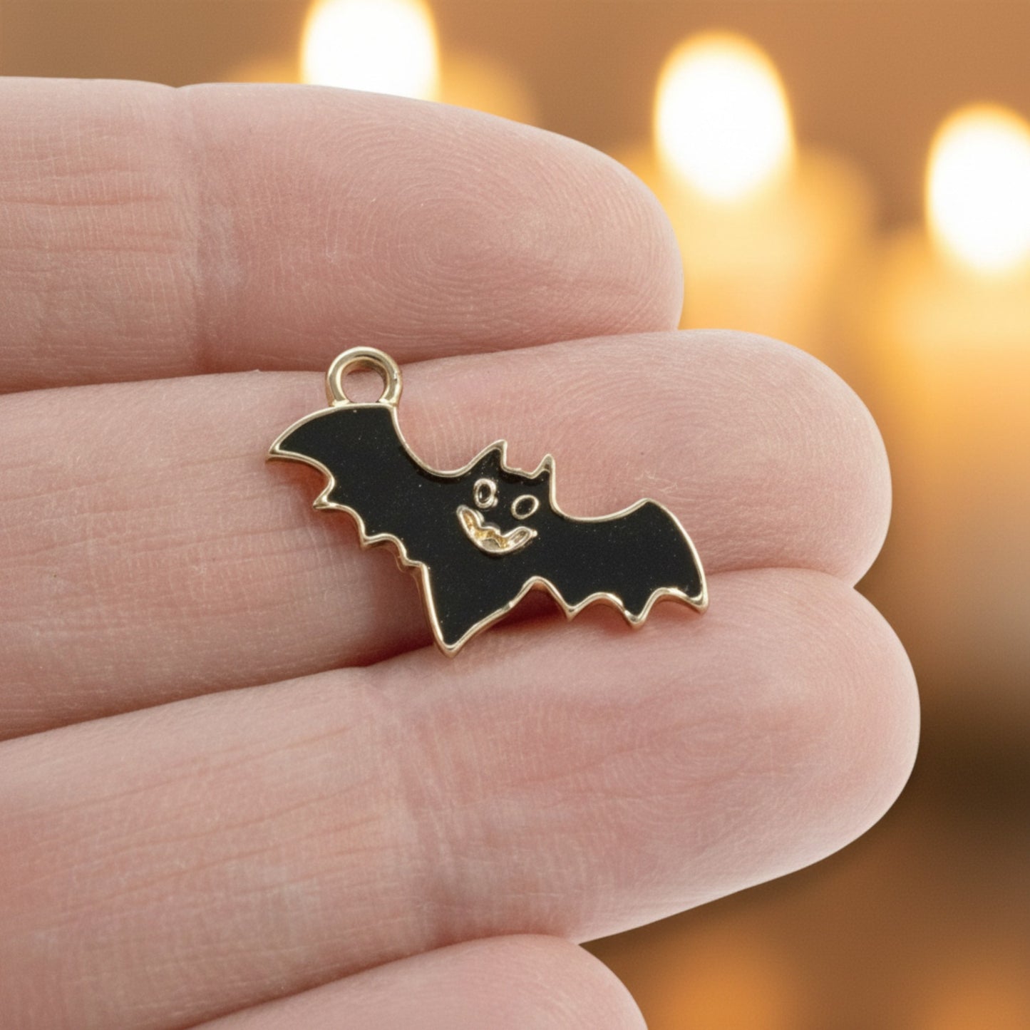 Hackberry Creek black enamel flying bat charm held in fingers with a gold-plated metal finish for gothic jewelry.