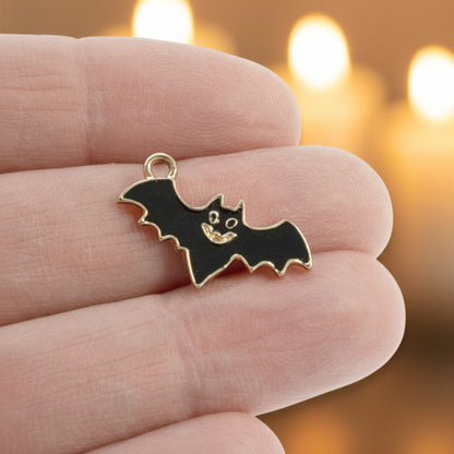 Hackberry Creek black enamel flying bat charm held in fingers with a gold-plated metal finish for gothic jewelry.