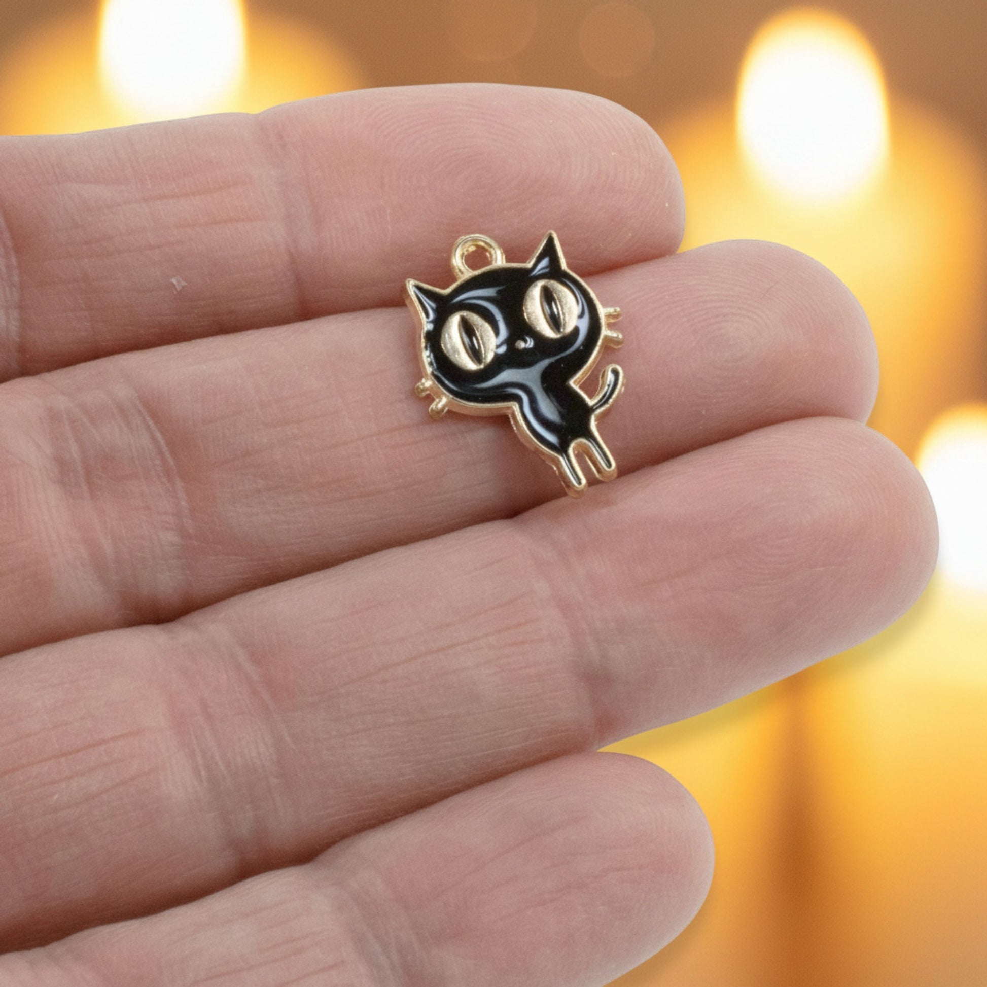 Hackberry Creek black enamel cat charm with gold-plated metal alloy held between fingers for jewelry making